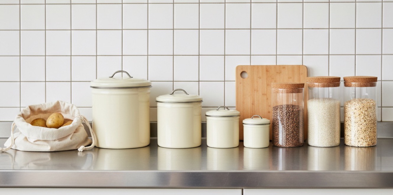 Enamel storage tins and glass pantry jars lined along an open pantry shelf